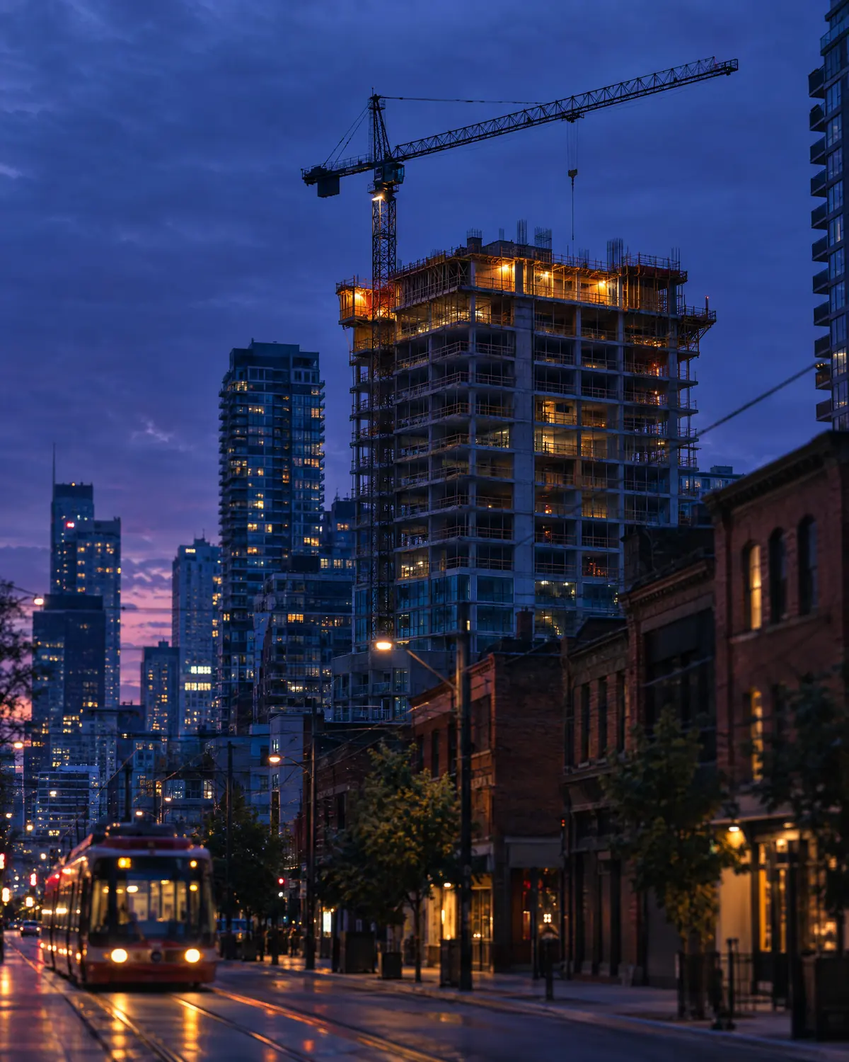 A residential tower under construction at dusk, with a tower crane above